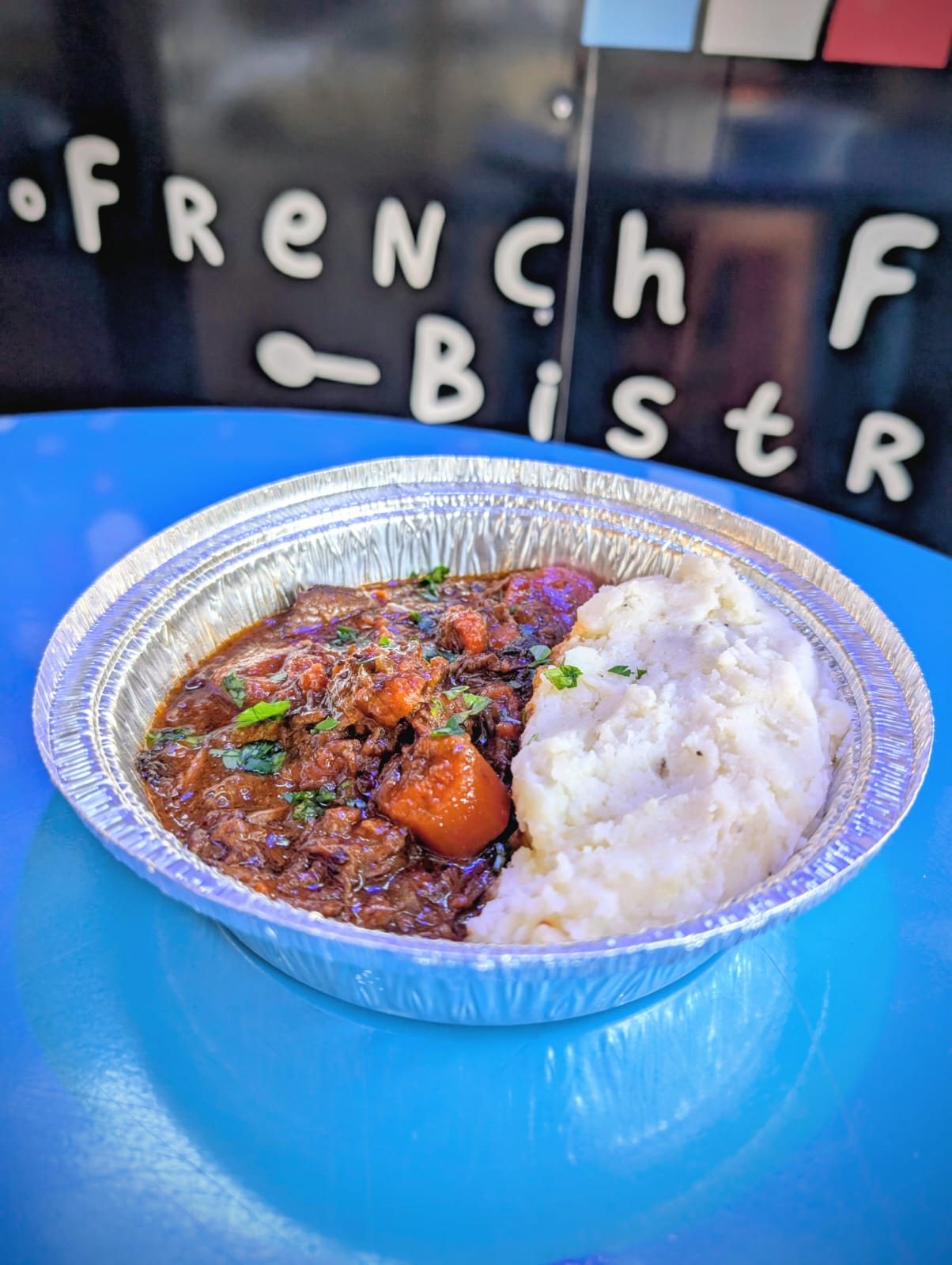 Beef Bourguignon with mashed potatoes, served in front of the Chez Leon truck signage.