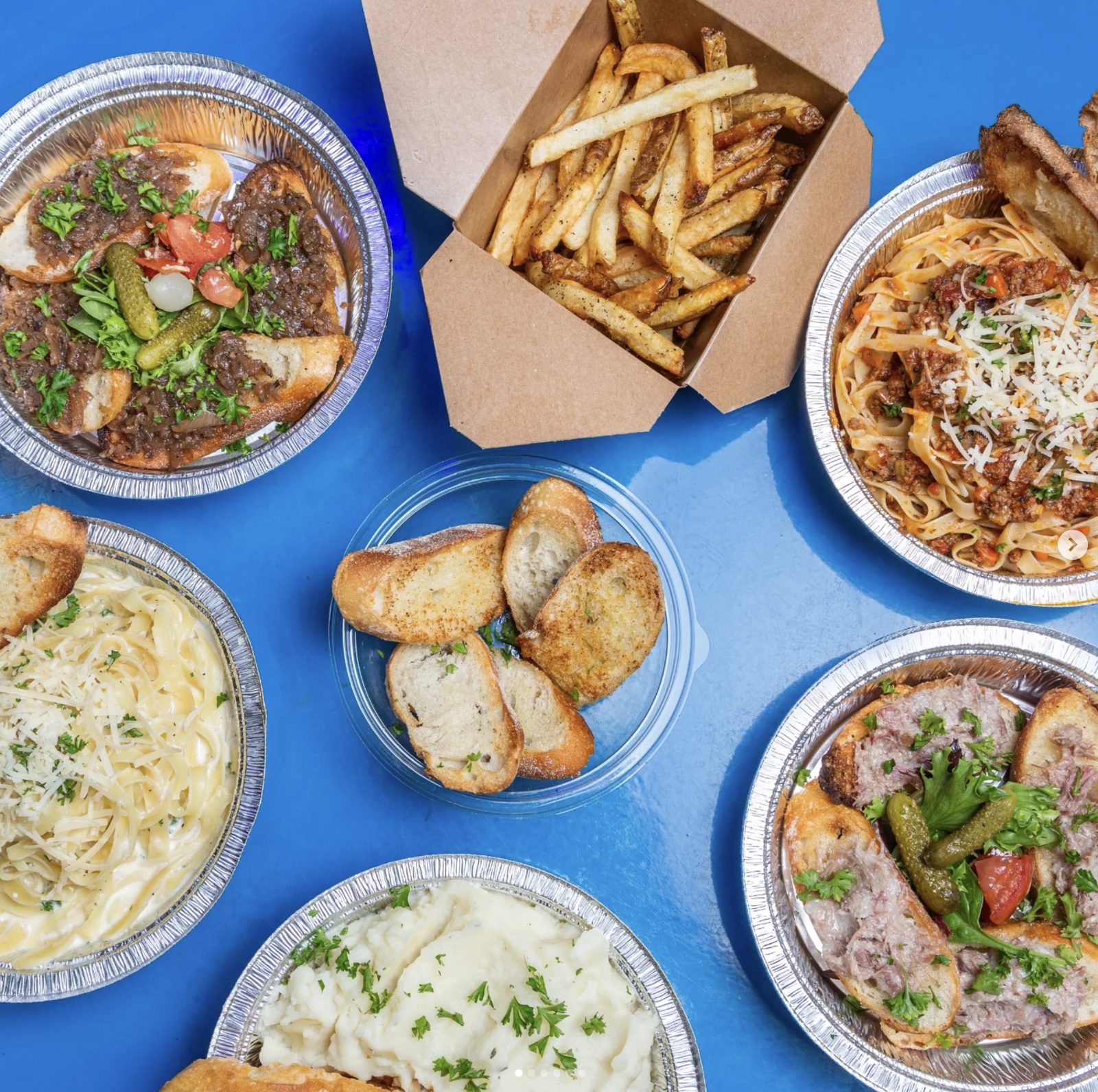 A spread of Chez Leon dishes including pasta, fries, and bruschetta on a blue table.