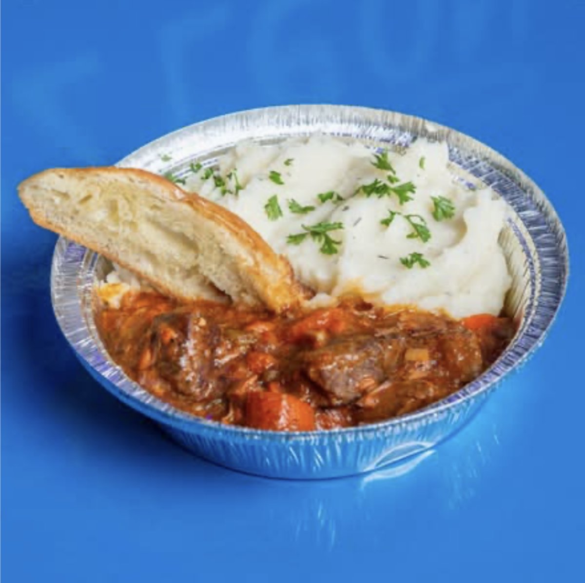 Beef Bourguignon with mashed potatoes and baguette, served in a to-go container.